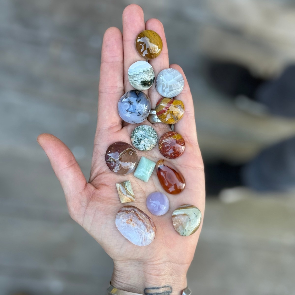 Hands and lapidary tools at a workbench with cut stones, from the Wolf Craft Cabochon Workshop product page on the school's official website.